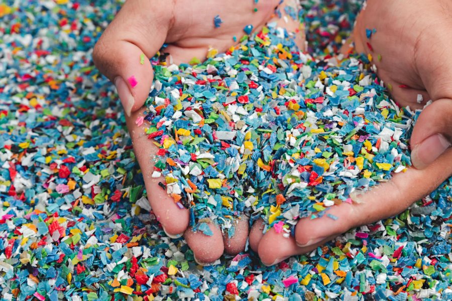 Hands holding shredded mixed-color plastic regrind